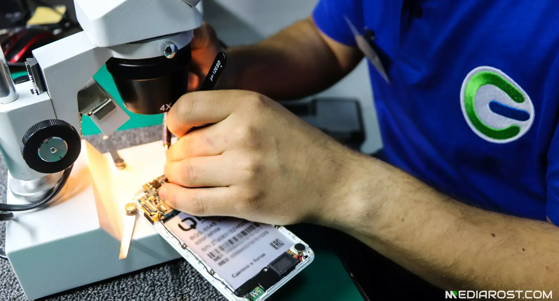 Мастер под микроскопом ремонтирует телефон